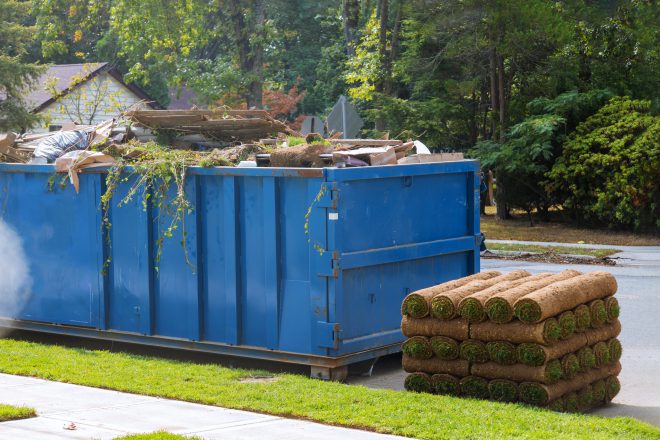 Lawn grass in rolls on pallets against of the street the rolled grass lawn ready for laying and loaded dumpster near construction urban landscape design